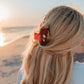 Person with long blonde hair and a red hair clip at the beach during sunset.