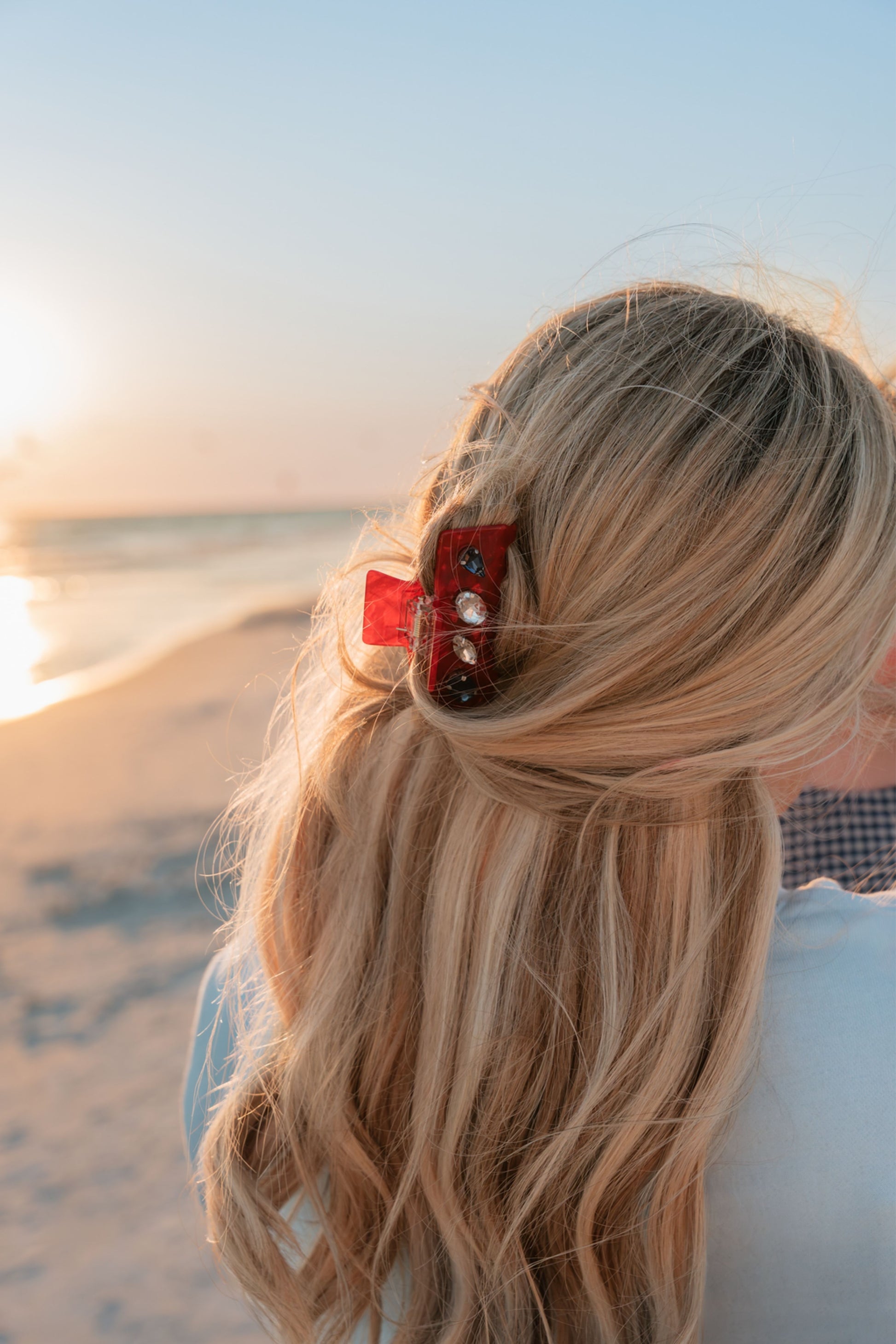 Person with long blonde hair and a red hair clip at the beach during sunset.