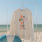 Beige sweatshirt with colorful text on a beach with a blue sky and ocean.