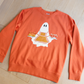Orange sweatshirt with a ghost design on a wooden floor