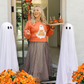 Woman in Halloween-themed outfit with ghosts and pumpkins on a decorated porch.