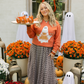 Woman standing on front porch in an orange sweatshirt with a ghost on the front holding a tray of caramel apples.