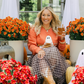 Woman sitting on a porch decorated for Halloween with flowers and ghost decorations.