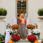Woman in a decorated front porch with Halloween decorations, including pumpkins and flowers.