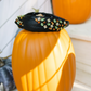 Decorative pumpkin with a black headband featuring colorful beads on a wooden surface.