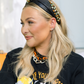Woman sitting wearing a black headband with mulitcolored jewels. 