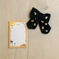 Black hair bow with candy corn design next to a Halloween-themed notepad on a wooden surface.