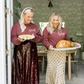 Two women in matching outfits holding plates of food in a home setting.
