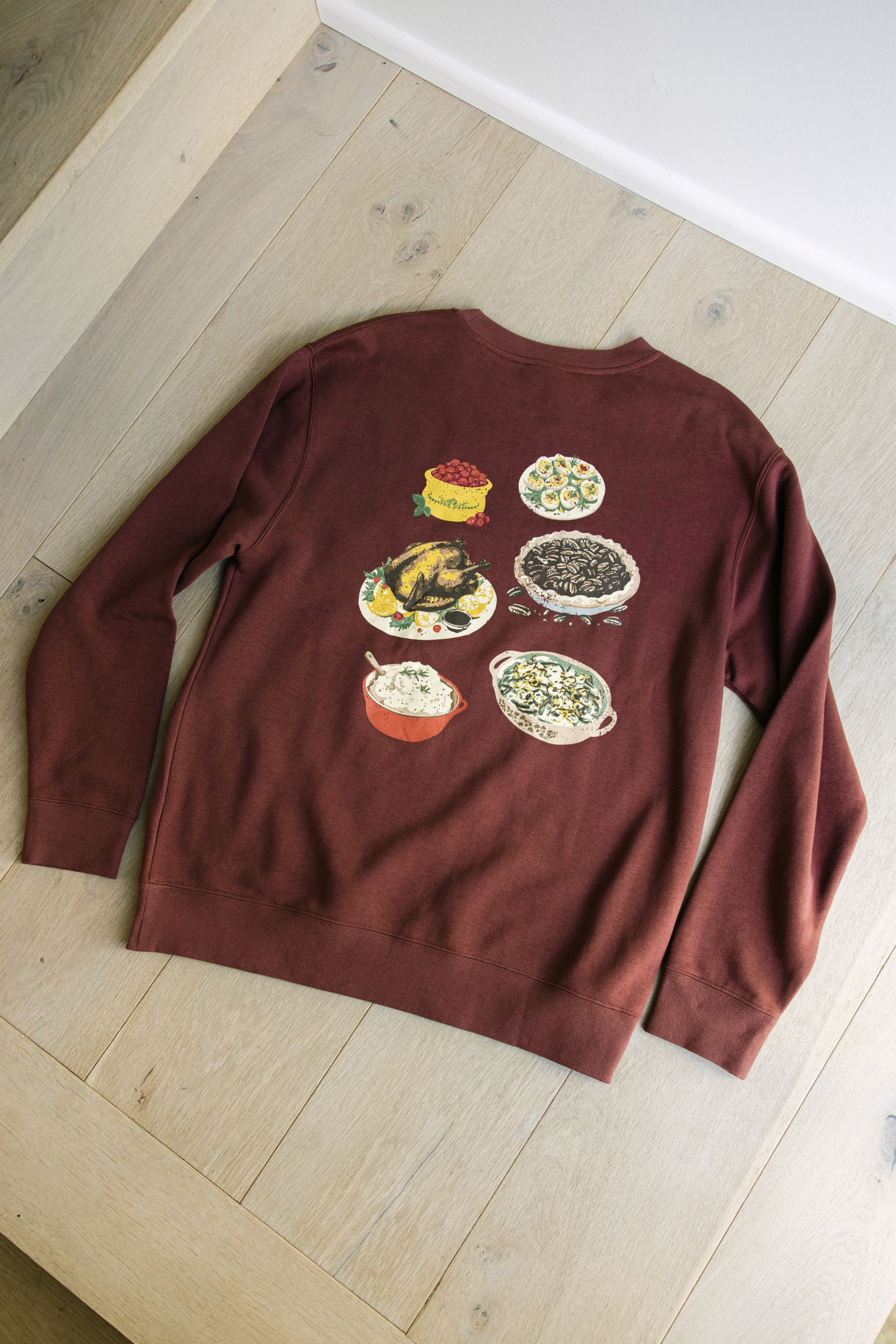 Maroon sweatshirt with food illustrations on a wooden surface
