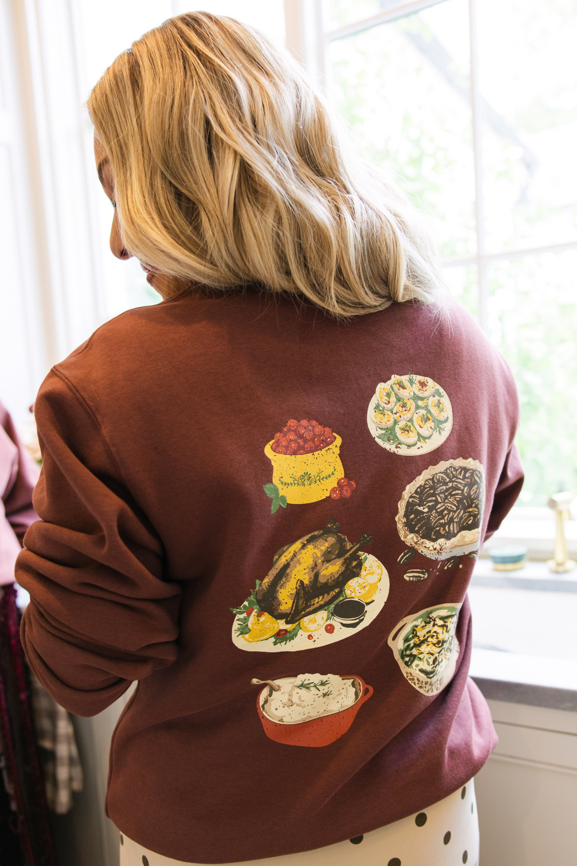 Person wearing a brown sweatshirt with food illustrations on the back.