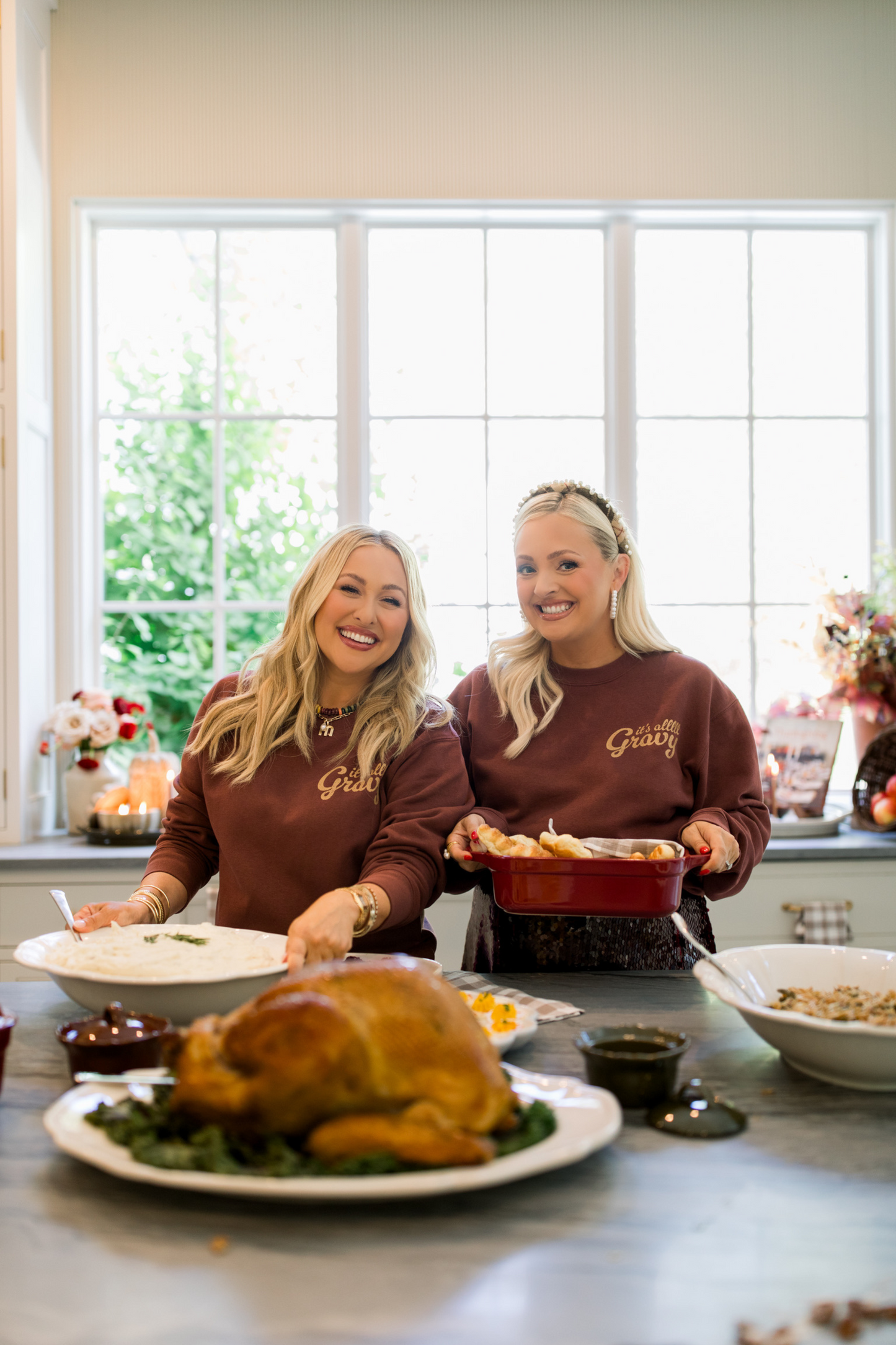 Two women in matching brown sweatshirts preparing a meal in a kitchen.
