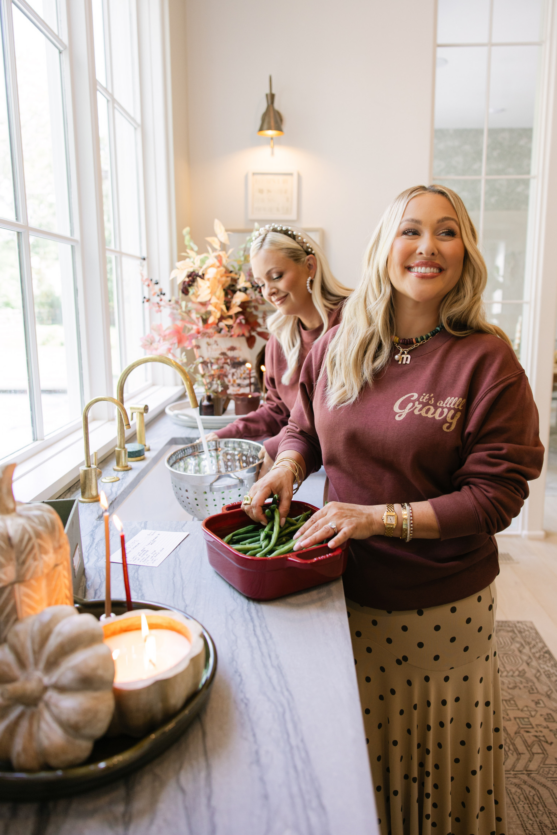 Two women in a kitchen preparing food, with one wearing a 'I am very grateful' sweater.