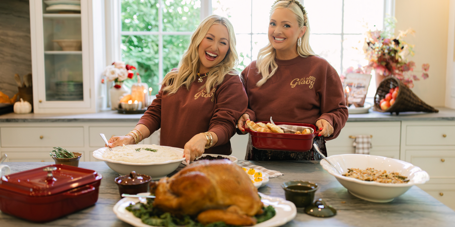 Two women in a kitchen preparing a meal with a roasted turkey and various dishes. Wearing its all gravy sweatshirt for Thanksgiving