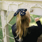 Child wearing a black hair bow with yellow and orange candy corn gems, standing in front of a white lattice structure.