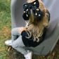 Child wearing a black bow with candy corn patterns, sitting on a gray slide outdoors.