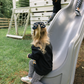 Child sliding down a playground slide with another child in the background.