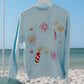 Light blue sweatshirt with festive designs on a hanger against a beach backdrop with a firework design and "Living Fully" text.