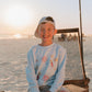 Child sitting on a beach chair at sunset with a light blue LFC kids sweatshirt and cap.