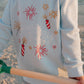 Child wearing a light blue LFC kids sweatshirt with firework designs on a beach.