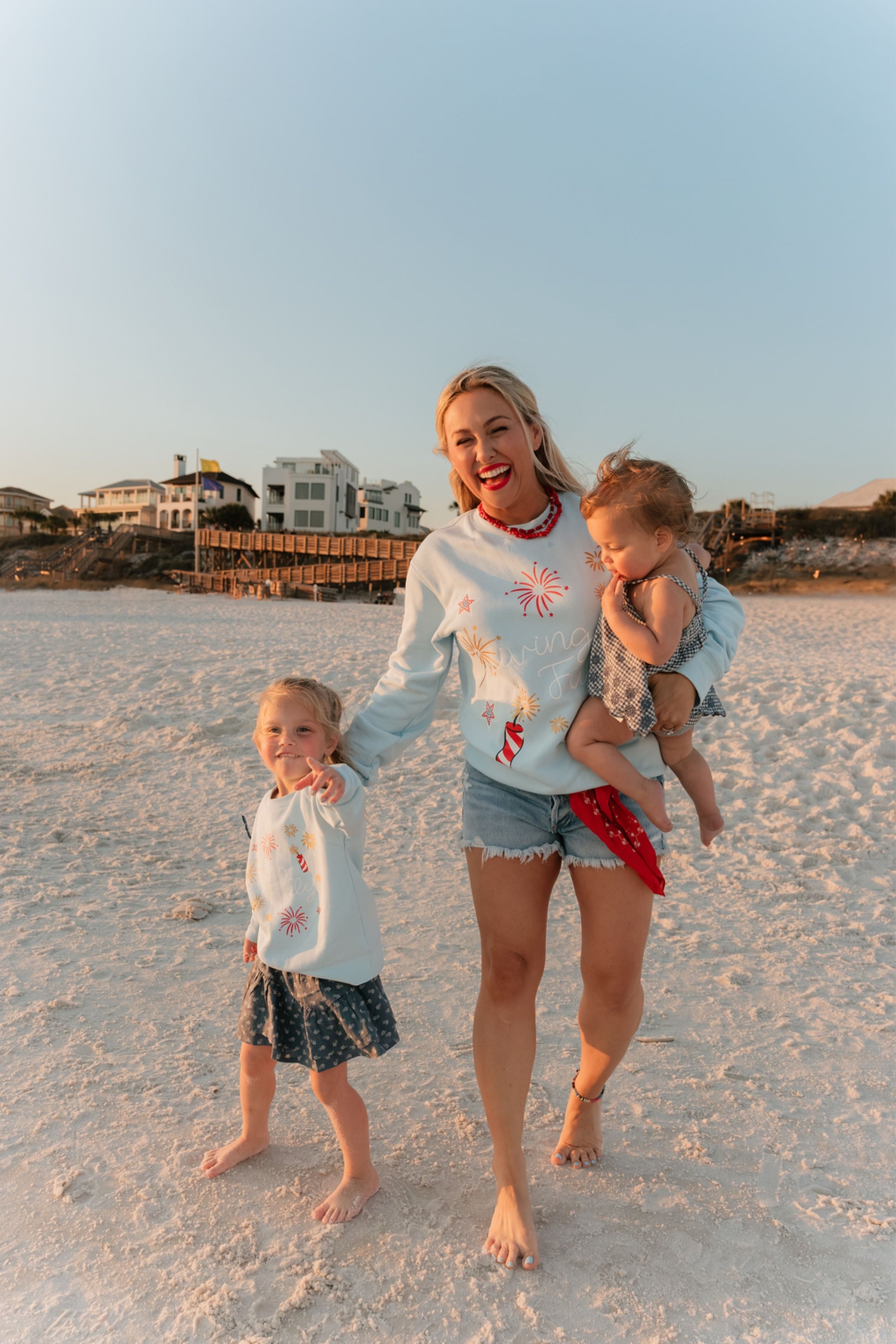 Woman with two children on a beach at sunset all wearing LFC sweatshirts.