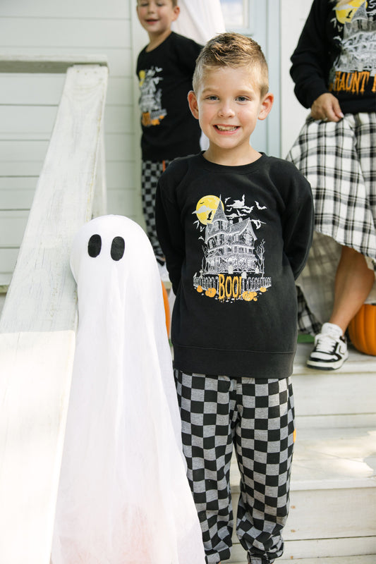 Child wearing a Halloween-themed shirt with a ghost figure on a staircase.