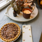 Pecan pie on a table with candles, a tray of flowers, and a card.