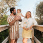 Family of three standing on a wooden deck with trees in the background.