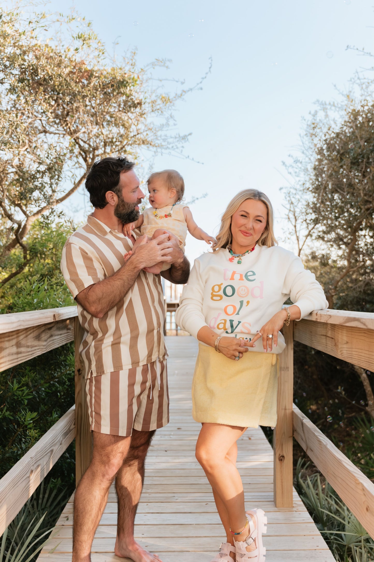 Family of three standing on a wooden deck with trees in the background.