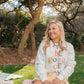Woman sitting on a blanket outdoors wearing a Living Fully Co. sweatshirt with colorful text.