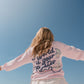 Person wearing a pink sweatshirt with text on the beach.