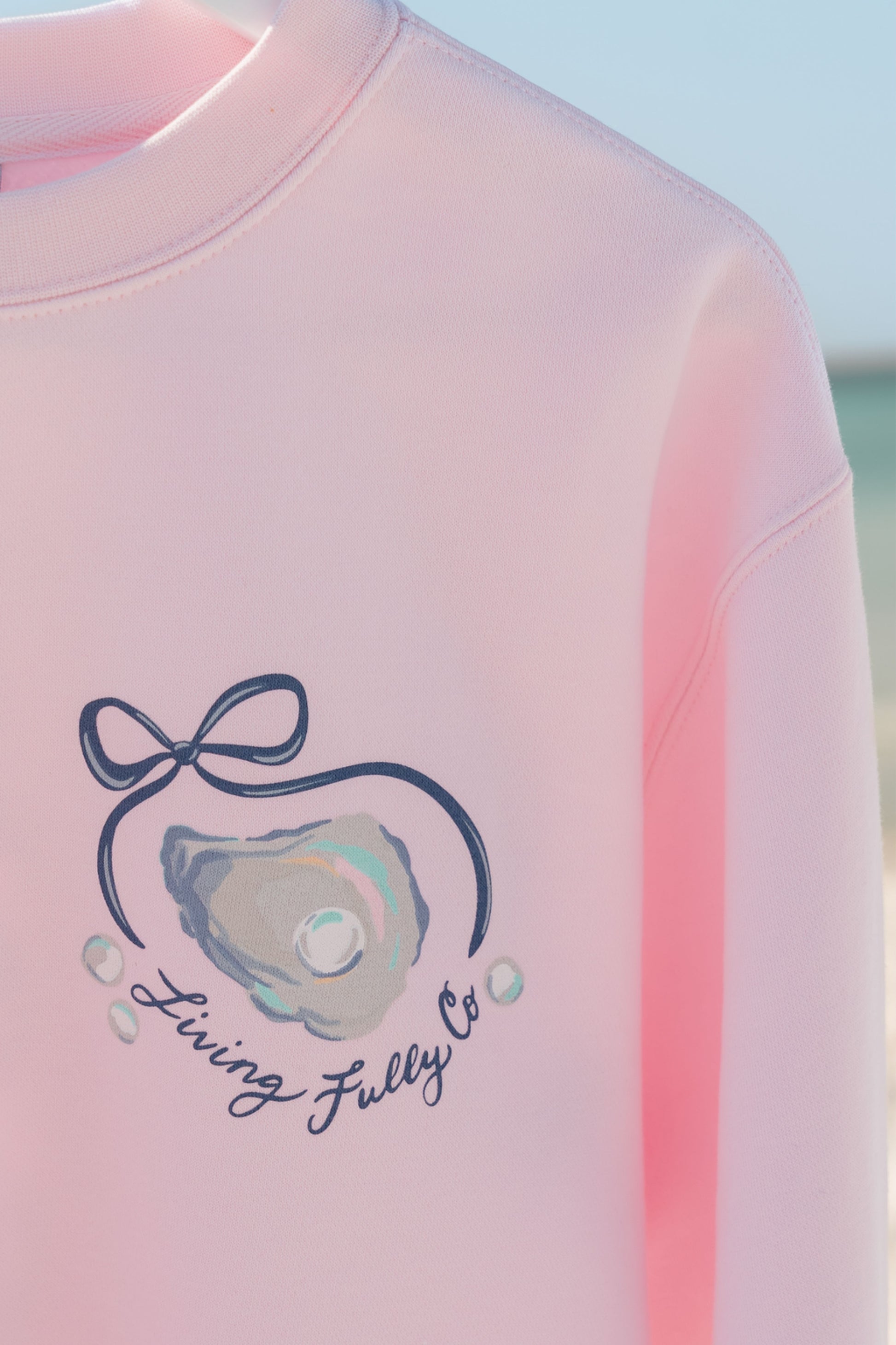 Pink sweatshirt with a Living Fully Co. logo and text on a light blue background.