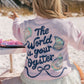 Person wearing a pink sweatshirt with 'The World is Your Oyster' text on a beach.