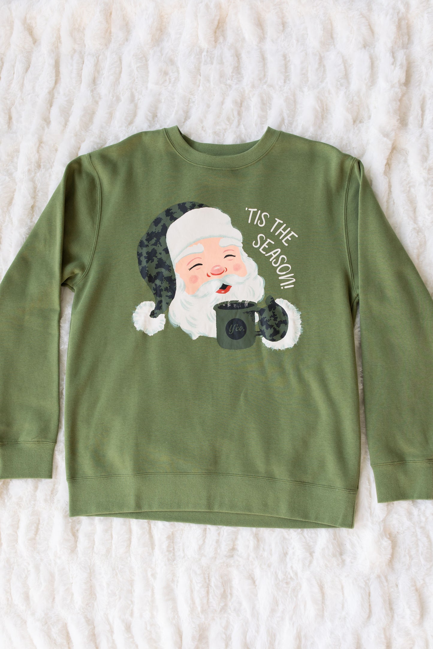 Green sweatshirt with Santa Claus graphic and text 'Tis the Season on a white textured background