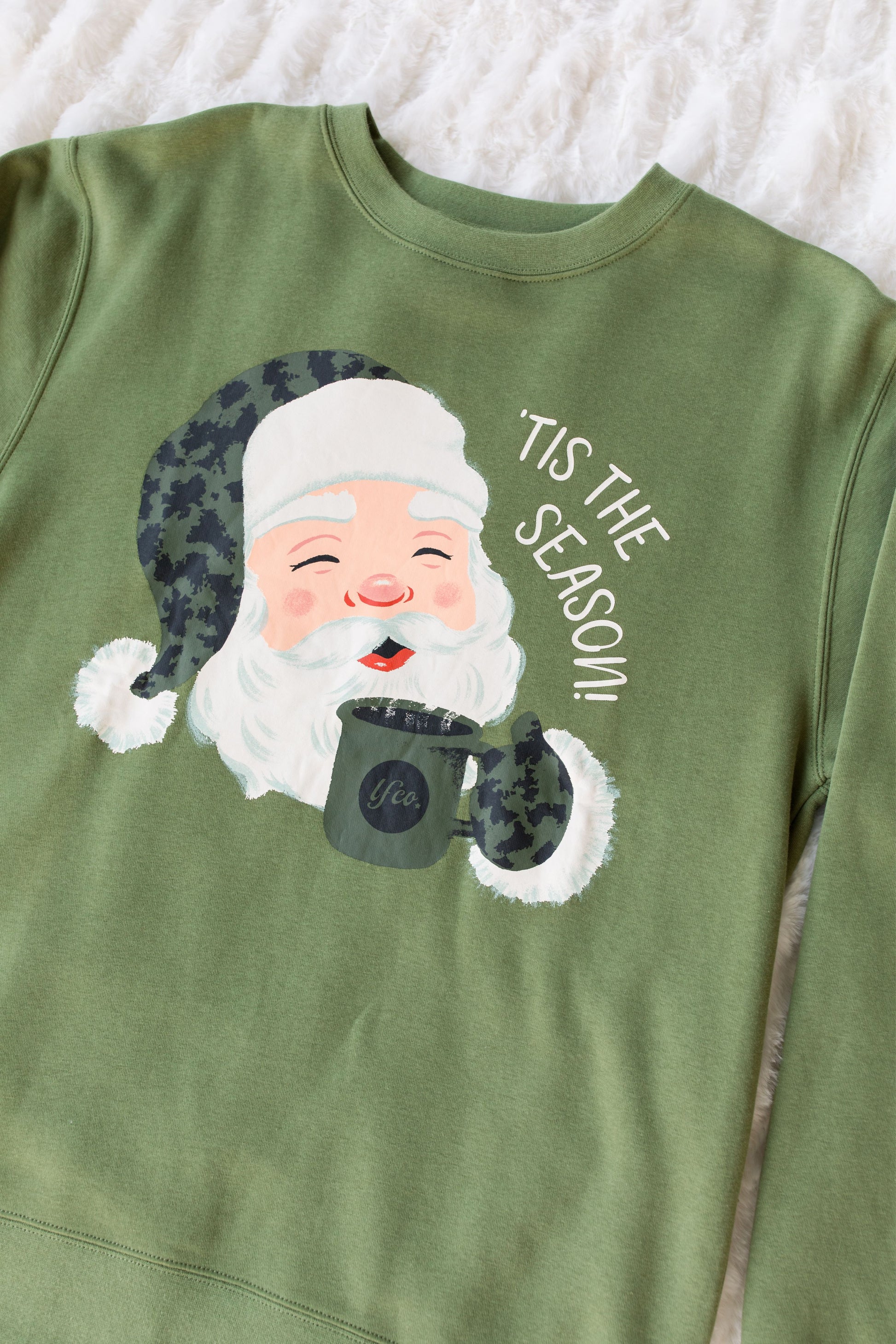 Green sweatshirt with a graphic of Santa Claus holding a mug and 'Tis the Season text on a white background.