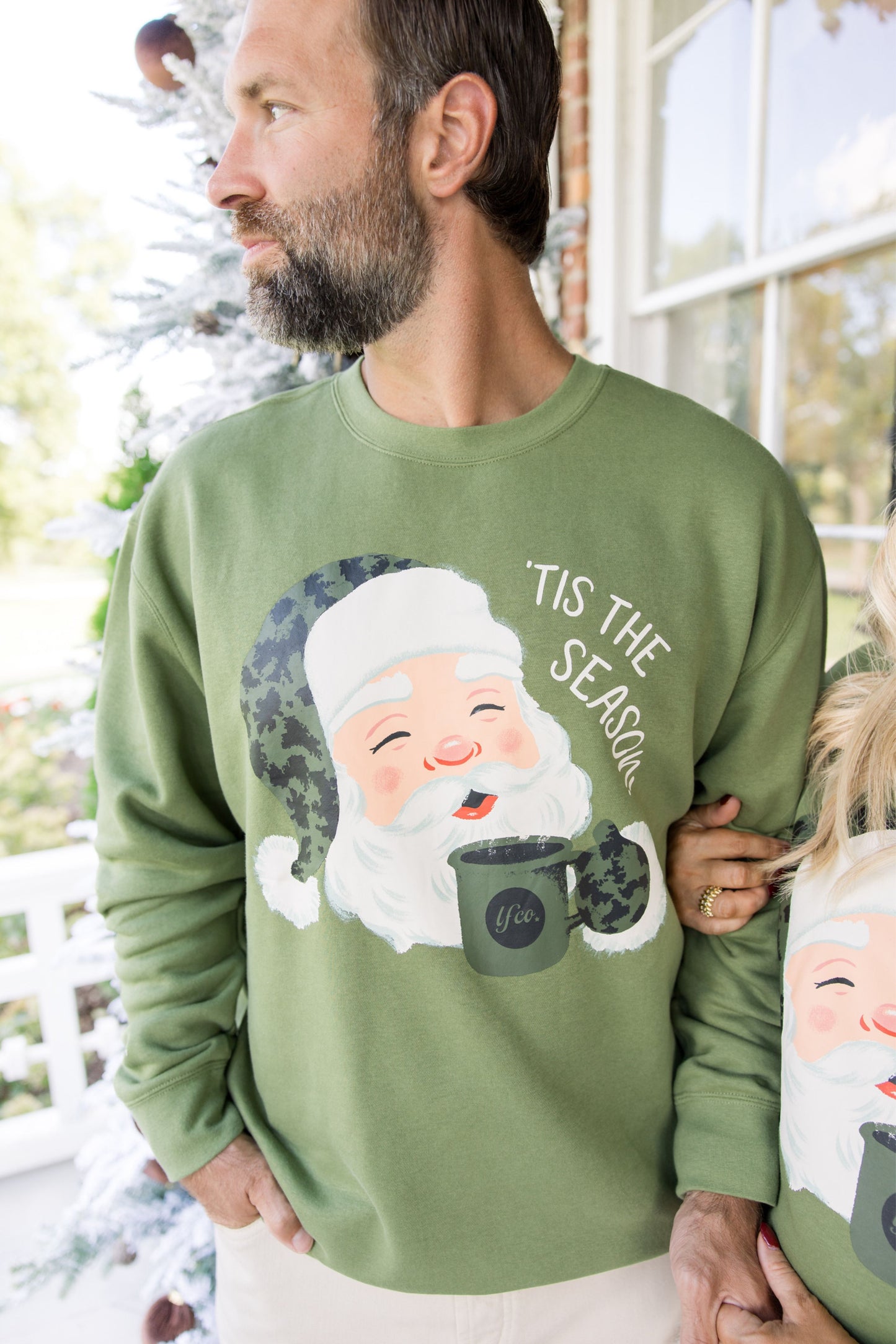 Man wearing a green sweater with a Santa Claus design and 'Tis the Season text.