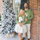 Couple standing in front of a decorated Christmas tree on a snowy porch.