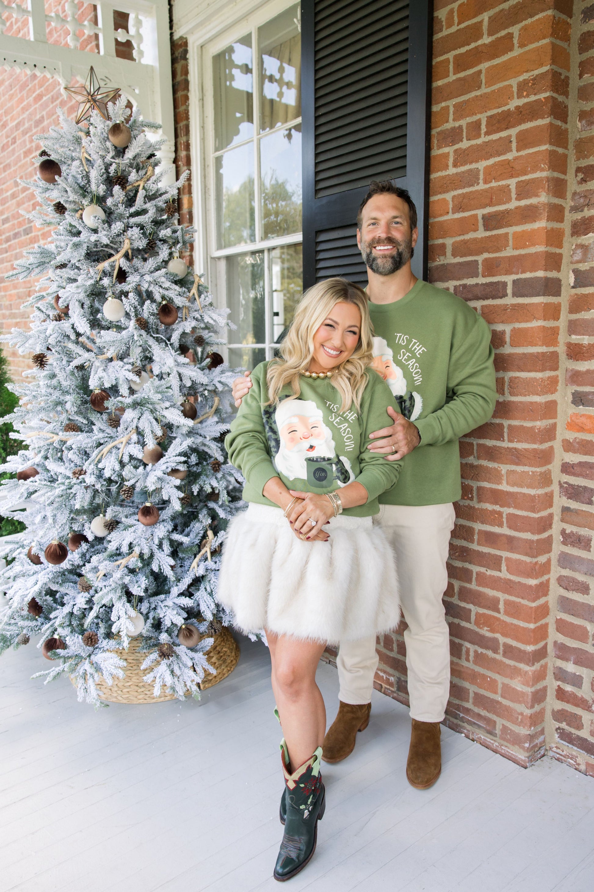 Couple standing in front of a decorated Christmas tree on a snowy porch.