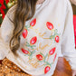 Person wearing a white sweatshirt with red and green designs in a festive setting