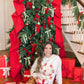 Woman sitting on the floor in front of a decorated Christmas tree with red ribbons and presents.