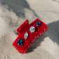 Red hair clip with gemstones on a sandy surface