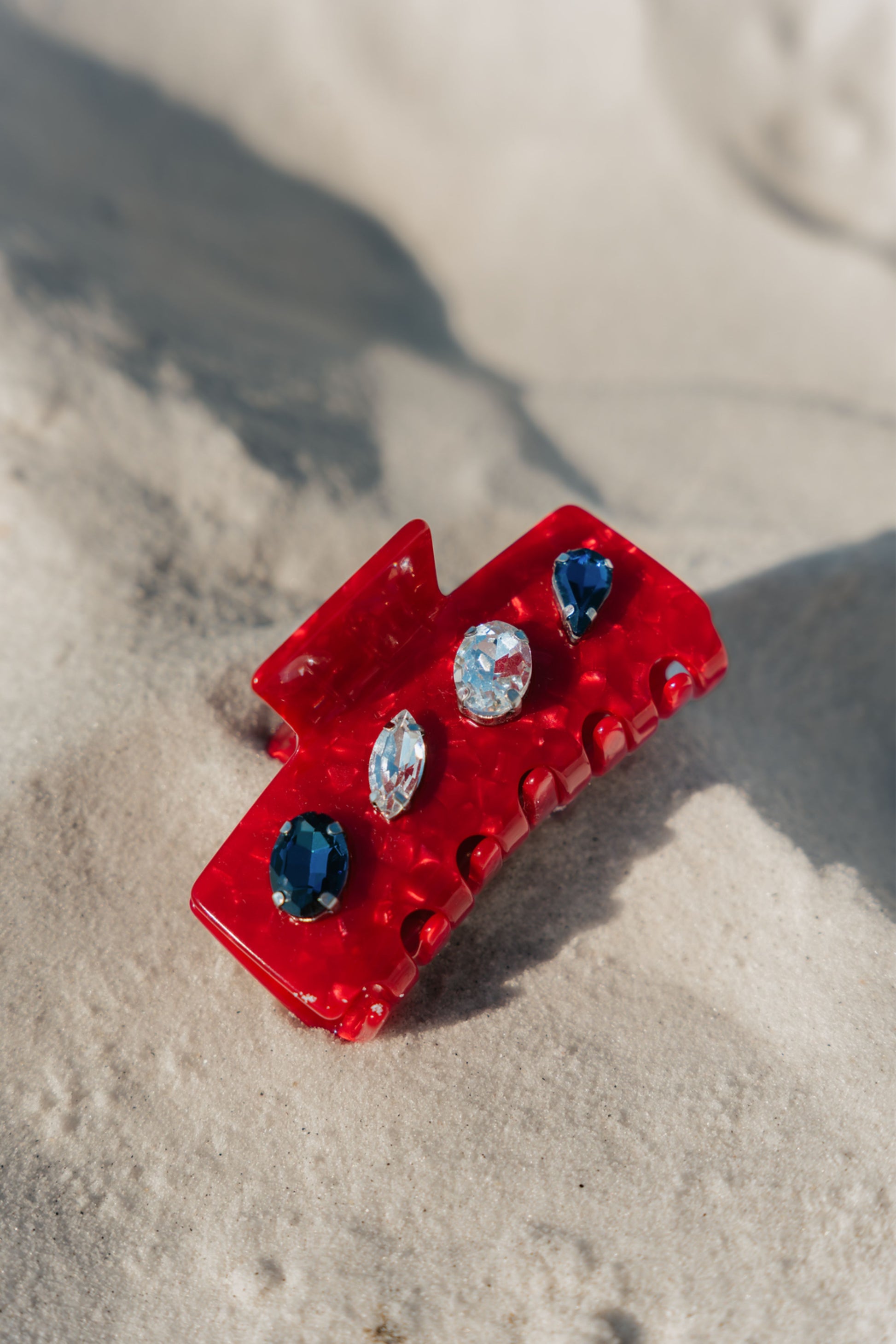 Red hair clip with gemstones on a sandy surface