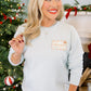 Woman wearing a light blue sweatshirt with a logo in front of a decorated Christmas tree.