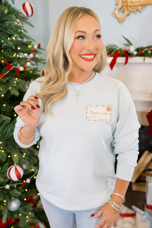 Woman wearing a light blue sweatshirt with a logo in front of a decorated Christmas tree.