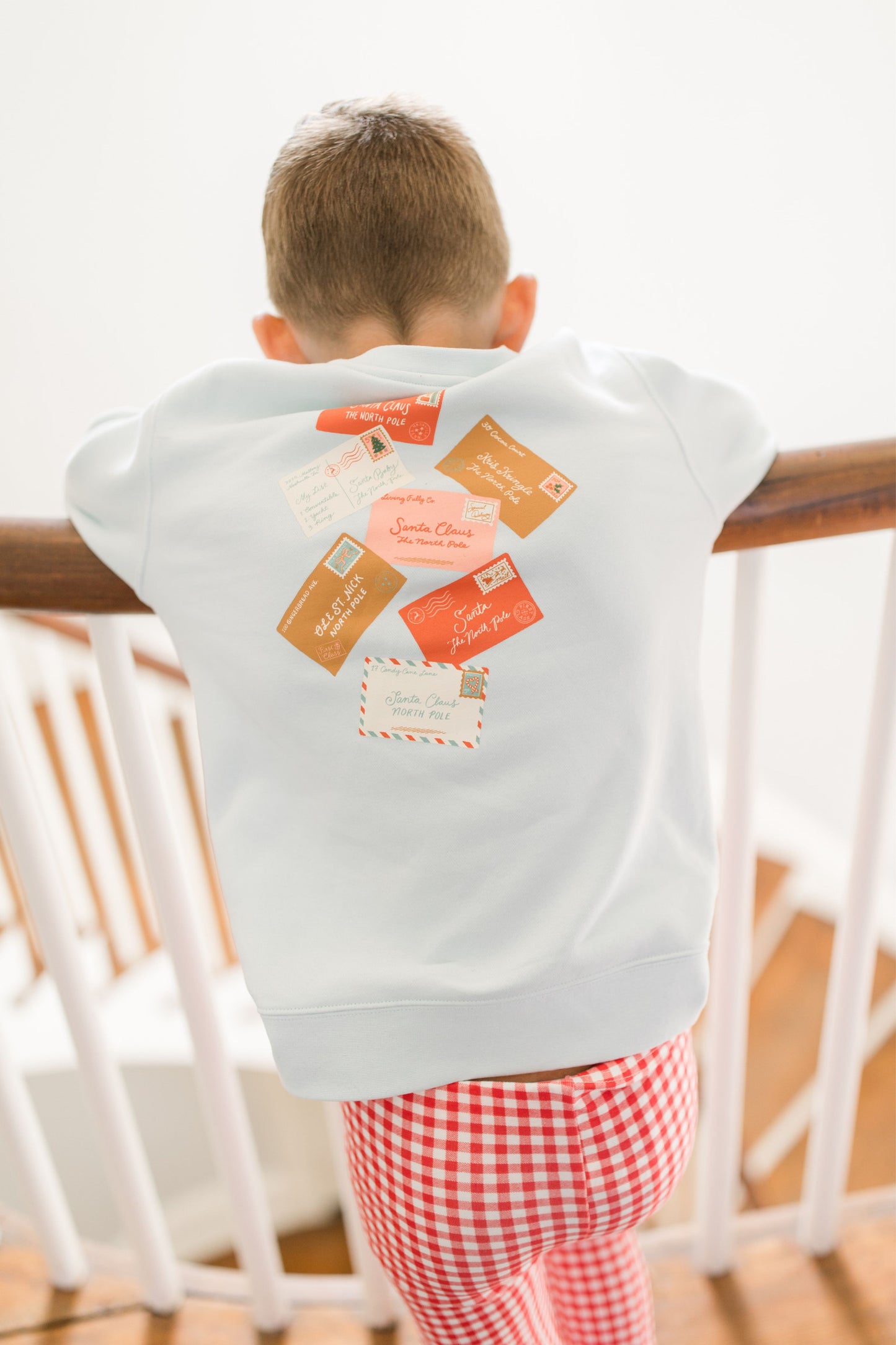 Child wearing a light blue sweatshirt with colorful printed postcard patches on the back, standing indoors.