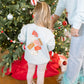 Child wearing a sweatshirt with colorful designs standing next to a decorated Christmas tree.
