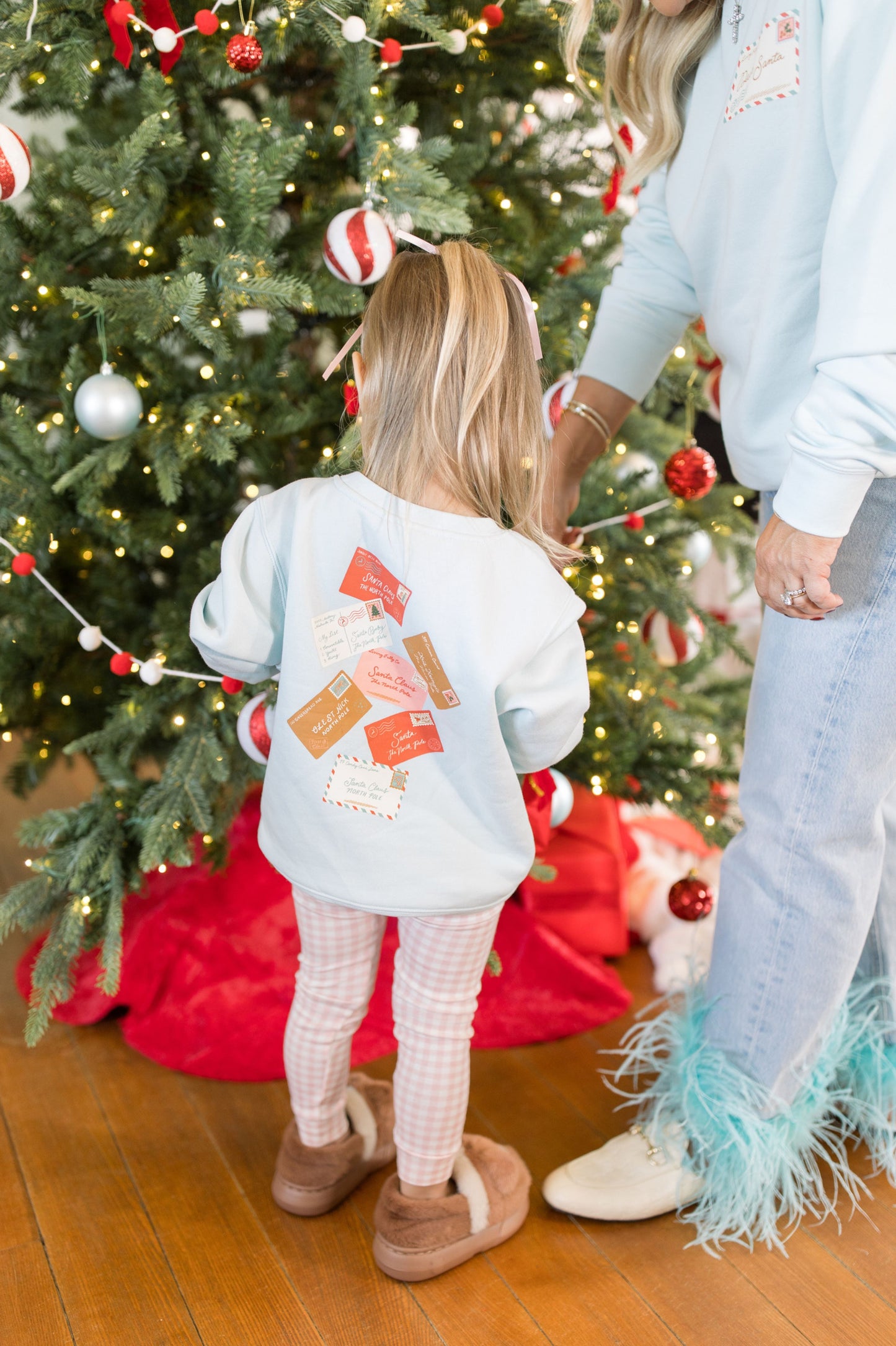 Child wearing a sweatshirt with colorful designs standing next to a decorated Christmas tree.