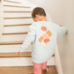 Child climbing a set of stairs wearing a light blue sweatshirt with a design on the back and red checkered pants.