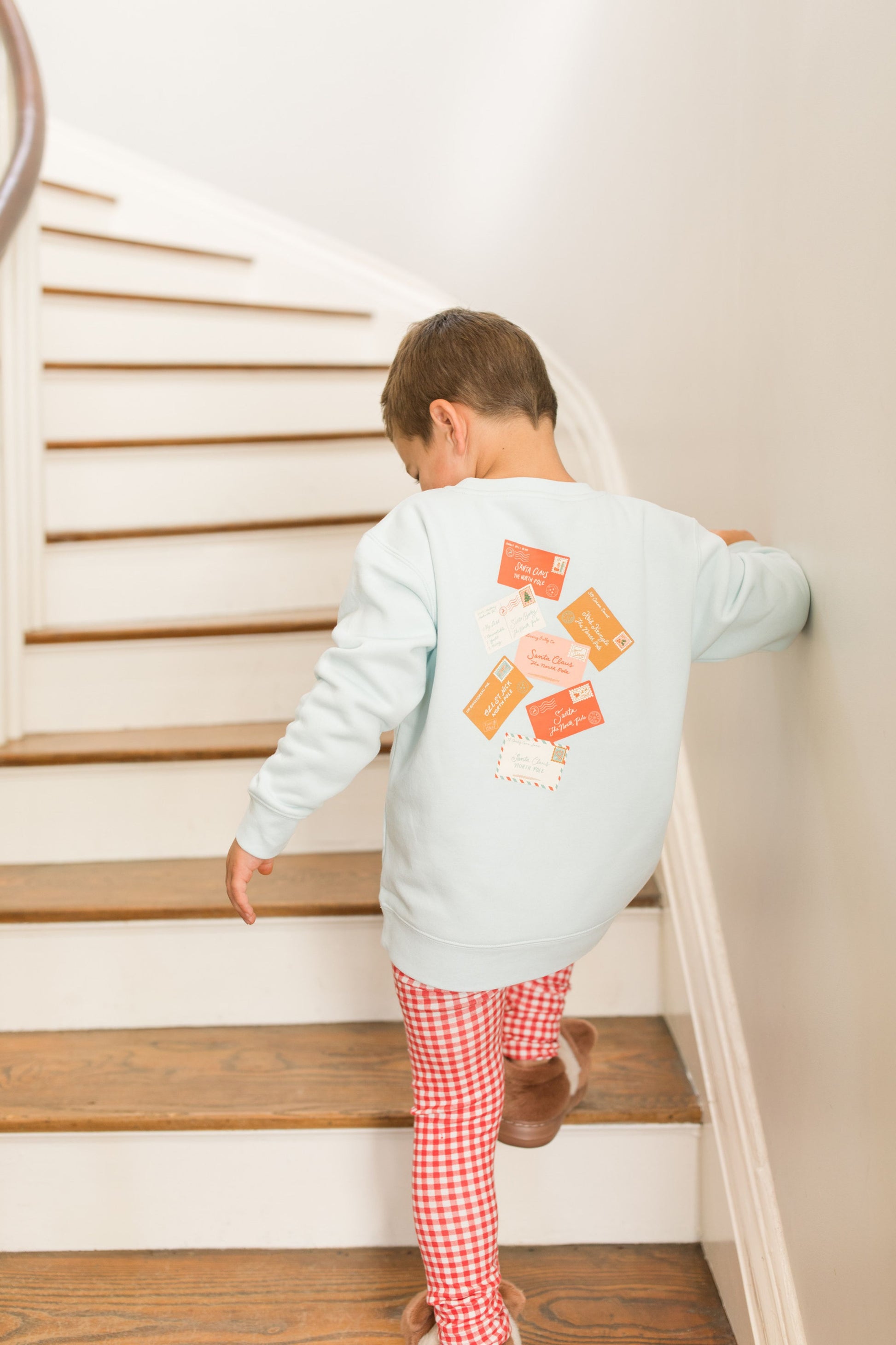 Child climbing a set of stairs wearing a light blue sweatshirt with a design on the back and red checkered pants.