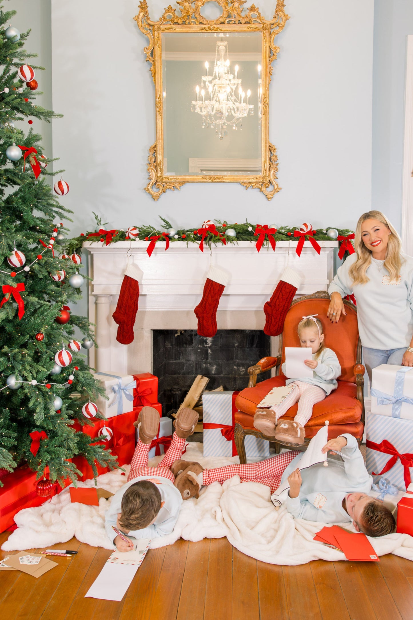 Family in a festive living room with Christmas decorations and children playing on the floor.