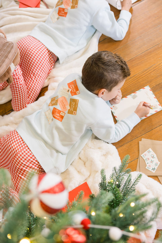 Child wearing a Christmas-themed sweatshirt with ornaments, sitting on the floor near a decorated Christmas tree.